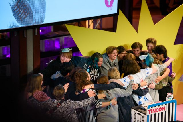 Eine Gruppe junger Menschen umarmt sich auf einer Bühne