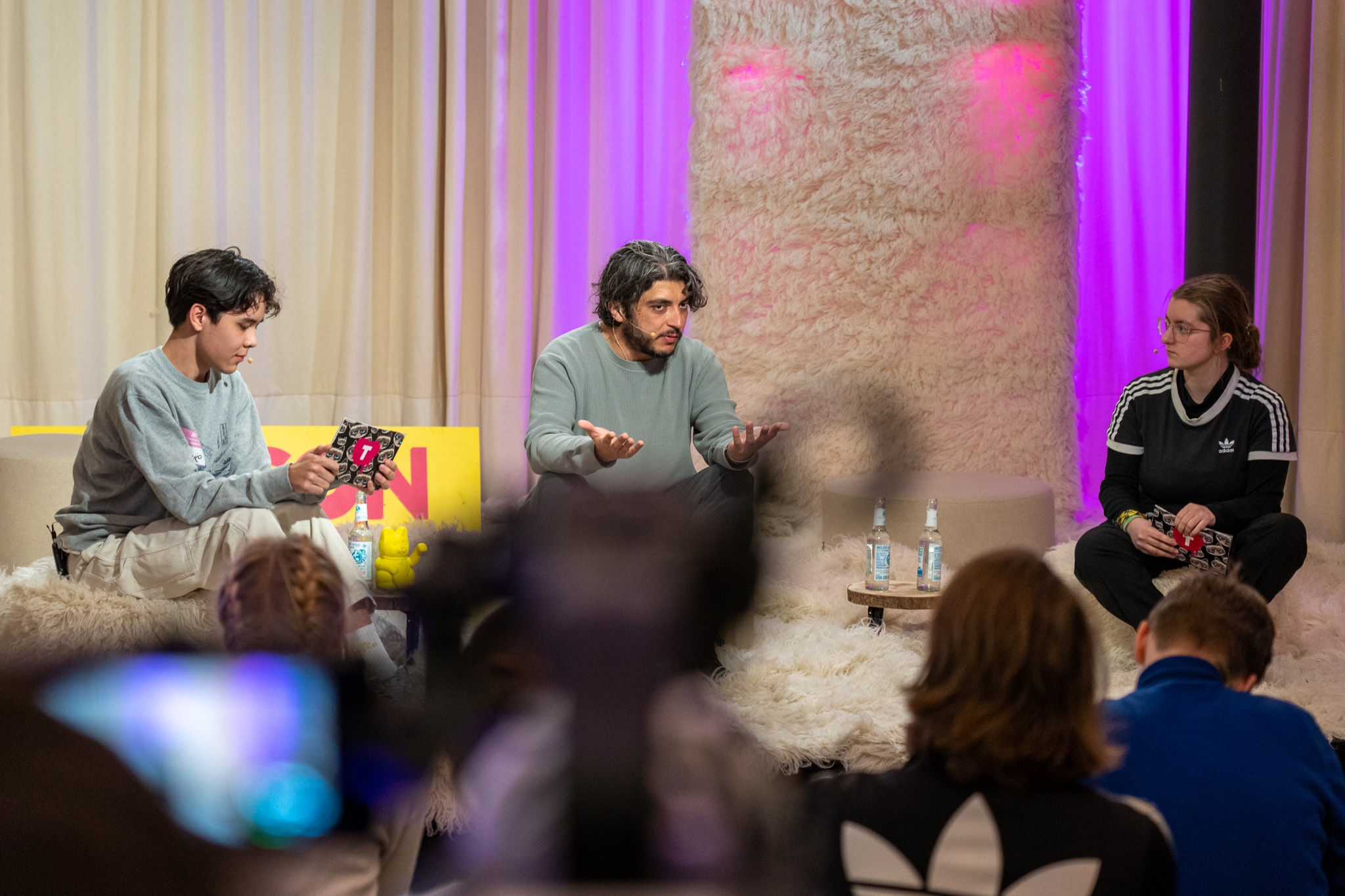 Khesrau Behroz im Interview auf der Bühne. Er wird von zwei jungen Moderator:innen befragt. 